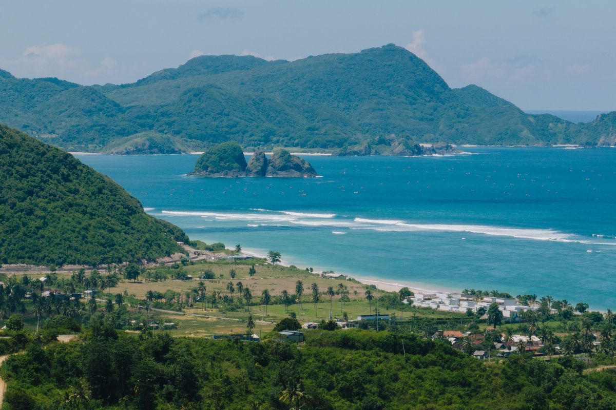 Green hills and coconut groves running down to a bay with rocky islets in South Lombok